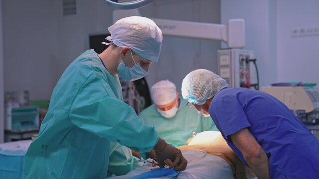 Group of medical specialists in the operating room. Doctors and nurses perform a plastic surgery to a patient in the hospital. Assistant with medical tools.