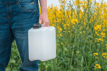 Rapeseed crop protection concept, female farmer agronomist holding jerry can bottle with pesticide