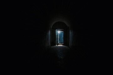Dark tunnel and the door  silhouette with a light behind it at the end.