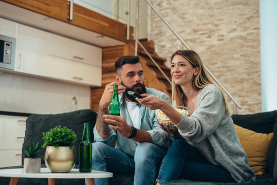 Young beautiful couple drinking beer and watching television at home