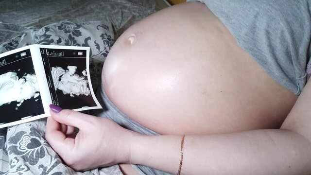 Beautiful pregnant woman feeling kick of baby. Mother-to-be watching sonogram picture