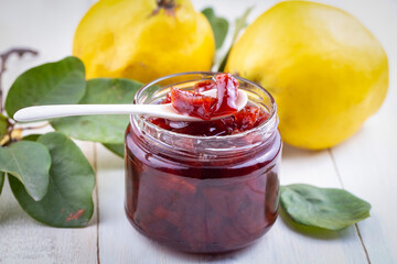 Homemade quince jam in a glass jar on an old wooden background. Fresh quince fruits and leaves and quince jam.