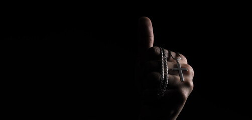 Praying with a rosary. hand of Catholic man with rosary on black background. Hands holding a silver...