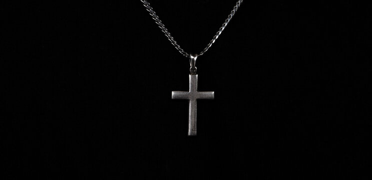Praying with a rosary. hand of Catholic man with rosary on black background. Hands holding a silver rosary or cross pendant of Jesus Christ. Crucifix and hand on black background. Praying God concept