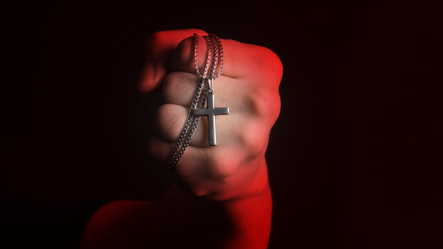 Praying with a rosary. hand of Catholic man with rosary on black background. Hands holding a silver rosary or cross pendant of Jesus Christ. Crucifix and hand on black background. Praying God concept
