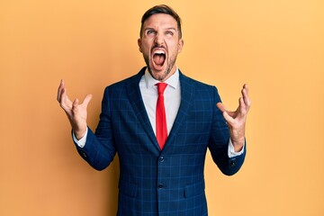 Handsome man with beard wearing business suit and tie crazy and mad shouting and yelling with aggressive expression and arms raised. frustration concept.