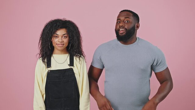 Gotcha. Positive young african american man and woman dancing and pointing fingers to camera, violet background