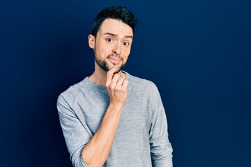 Young hispanic man wearing casual clothes looking confident at the camera with smile with crossed arms and hand raised on chin. thinking positive.