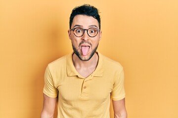 Young hispanic man wearing casual clothes and glasses sticking tongue out happy with funny...