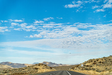 Two lane road in the arid Sierra Nevada's leading to mountains against blue sky