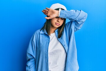 Young latin woman wearing cute wool cap covering eyes with arm, looking serious and sad. sightless, hiding and rejection concept