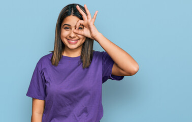 Obraz na płótnie Canvas Young hispanic girl wearing casual purple t shirt doing ok gesture with hand smiling, eye looking through fingers with happy face.