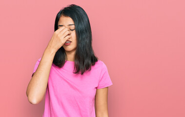 Beautiful asian young woman wearing casual pink t shirt tired rubbing nose and eyes feeling fatigue and headache. stress and frustration concept.