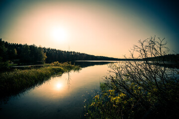 Sunset over the forest lake. View from the shore level, image vignetting and the orange-blue toning