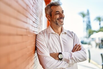 Middle age grey-haired man smiling happy with arms crossed gesture at the city.