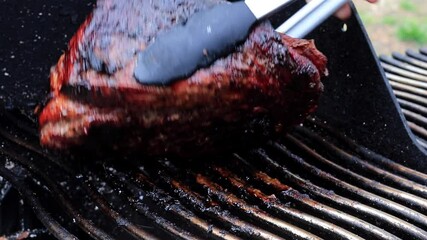 Turning side of pork shoulder piece of meat grilling on the smoker