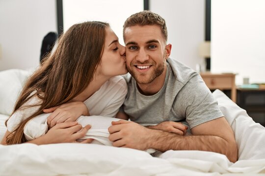 Young caucasian couple smiling happy and kissing on the bed at home.