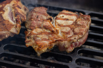 
A large pork neck steak is fried on a thick cast iron wire rack. Angle view