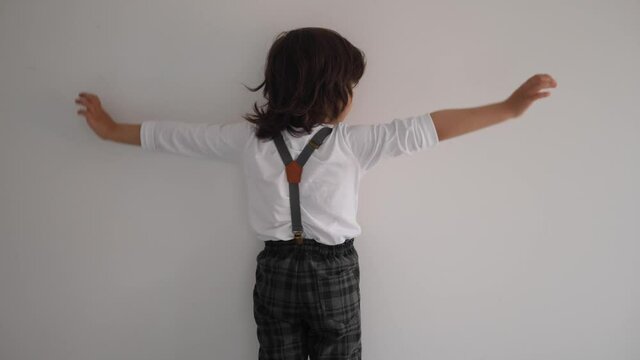 boy in a white T-shirt stands with his back to the white wal
