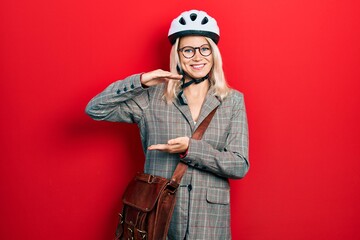 Beautiful caucasian blonde business woman wearing bike helmet gesturing with hands showing big and large size sign, measure symbol. smiling looking at the camera. measuring concept.