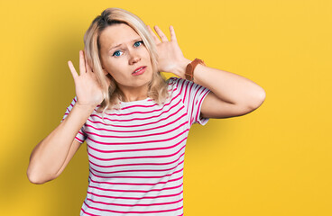 Young caucasian woman wearing casual clothes trying to hear both hands on ear gesture, curious for gossip. hearing problem, deaf