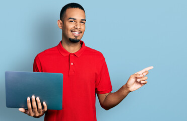 Young african american man working using computer laptop smiling happy pointing with hand and finger to the side