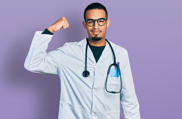 Young african american man wearing doctor uniform and stethoscope strong person showing arm muscle, confident and proud of power