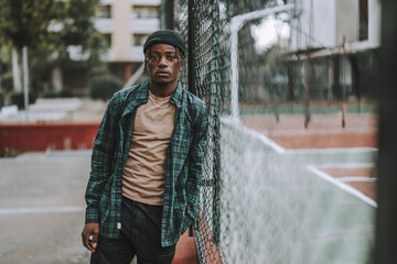 Handsome and stylish Spanish man leaning the chain-link fence and posing