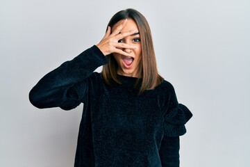Young brunette girl wearing elegant fashion sweater peeking in shock covering face and eyes with hand, looking through fingers afraid