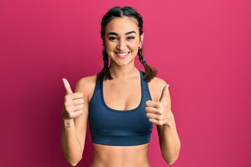 Young brunette girl wearing sportswear and braids success sign doing positive gesture with hand, thumbs up smiling and happy. cheerful expression and winner gesture.