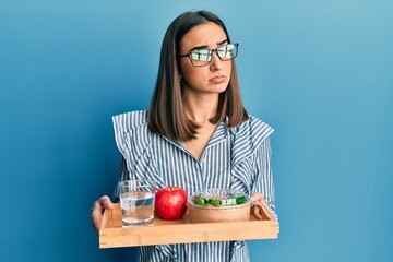 Young brunette girl holding tray with healthy lunch clueless and confused expression. doubt concept.