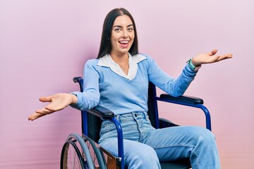 Beautiful woman with blue eyes sitting on wheelchair smiling cheerful offering hands giving...