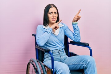 Beautiful woman with blue eyes sitting on wheelchair pointing aside worried and nervous with both...
