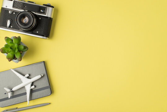 Top view photo of plant camera pen and plane model on grey diary on isolated pastel yellow background with copyspace
