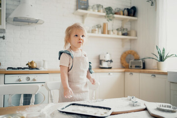 Cooking girl child playing in the kitchen. Makes pastry dough, pasta, pizza, spaghetti, dessert. The little chef is the host on the table with the ingredients flour and sugar for a cake or sweet.