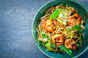 Modern style traditional Thai phak kung curry with barbecue king prawns and noodles as top view in Nordic design bowl with copy space left