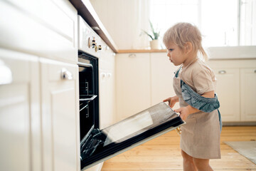 Independent child in the apartment. The blonde girl prepares pastries, cake, dessert for the holiday in the oven in the kitchen.