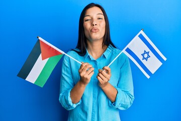 Young latin woman holding palestine and israel flags looking at the camera blowing a kiss being lovely and sexy. love expression.