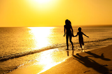 Silhouettes of two happy children playing and running along the seashore at sunset