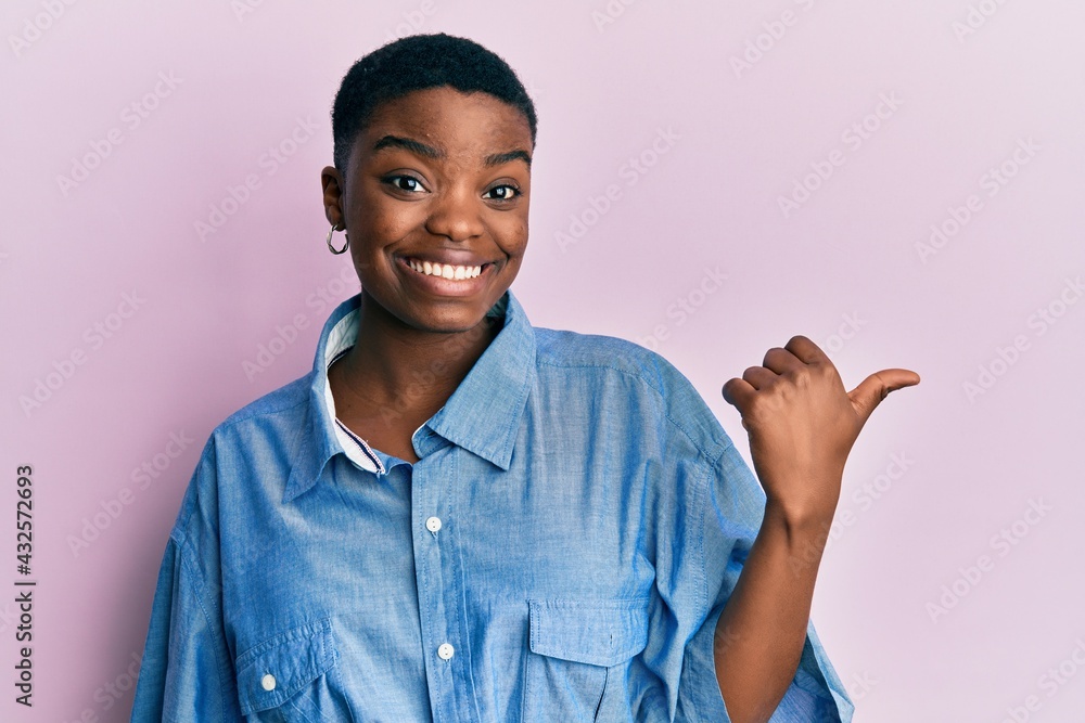 Wall mural young african american woman wearing casual clothes smiling with happy face looking and pointing to 