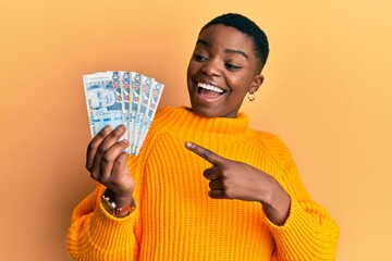 Young african american woman holding peruvian sol banknotes smiling happy pointing with hand and finger - obrazy, fototapety, plakaty
