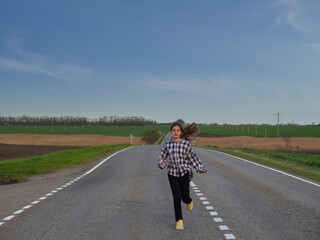 Fototapeta premium A teenage girl runs along a rural country road among fields. There is an expression of effort on the face