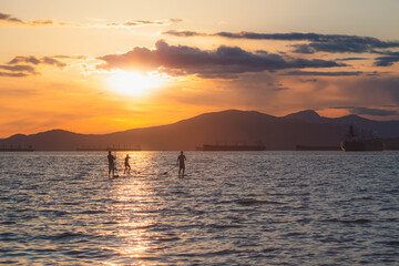 Silhouette of paddle boarders during sunset golden hour light on on open Pacific ocean water at Kitsilano Beach on an idyllic summer evening in Vancouver, B.C., Canada.
