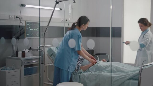 Patient sitting in bed having respiratory illness while medical nurse monitoring heart pulse in hospital ward. Sick manresting in bed while doctor analyzing pulse using medical oximeter