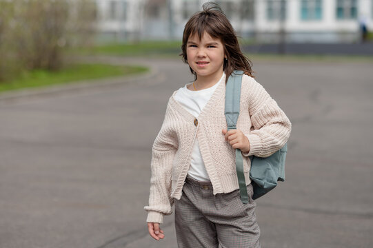 happy girl a schoolgirl of 8 years of European appearance with a backpack is walking in the school yard in the afternoon on the street looking at the camera closeup. High quality photo