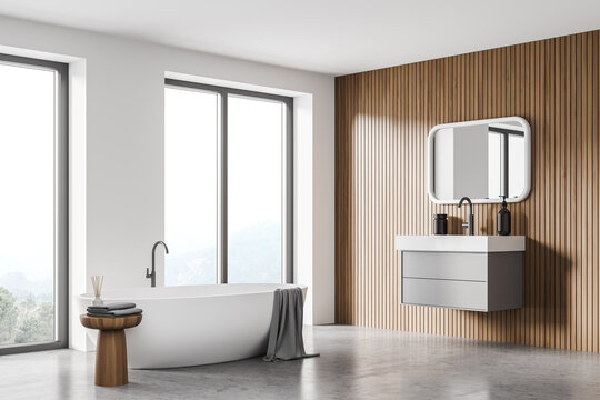 White and wooden bathroom interior with sink and mirror, bathtub near window
