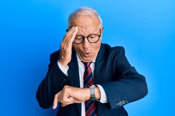 Senior caucasian man wearing business suit and tie looking at the watch time worried, afraid of getting late