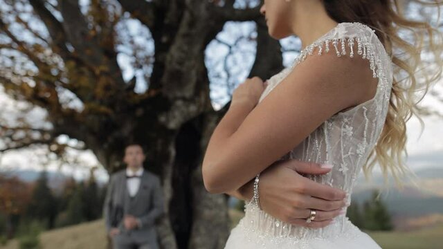 Newlyweds. Lovely young bride and groom stay together on mountain slope hill. Goosebumps on brides hand skin. Wedding happy family couple. Man looking at woman in love. Bride in gorgeous wedding dress