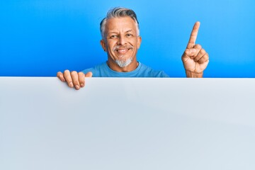 Middle age grey-haired man holding blank empty banner smiling happy pointing with hand and finger to the side
