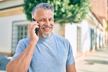 Middle age hispanic grey-haired man smiling happy talking on the smartphone at the city.